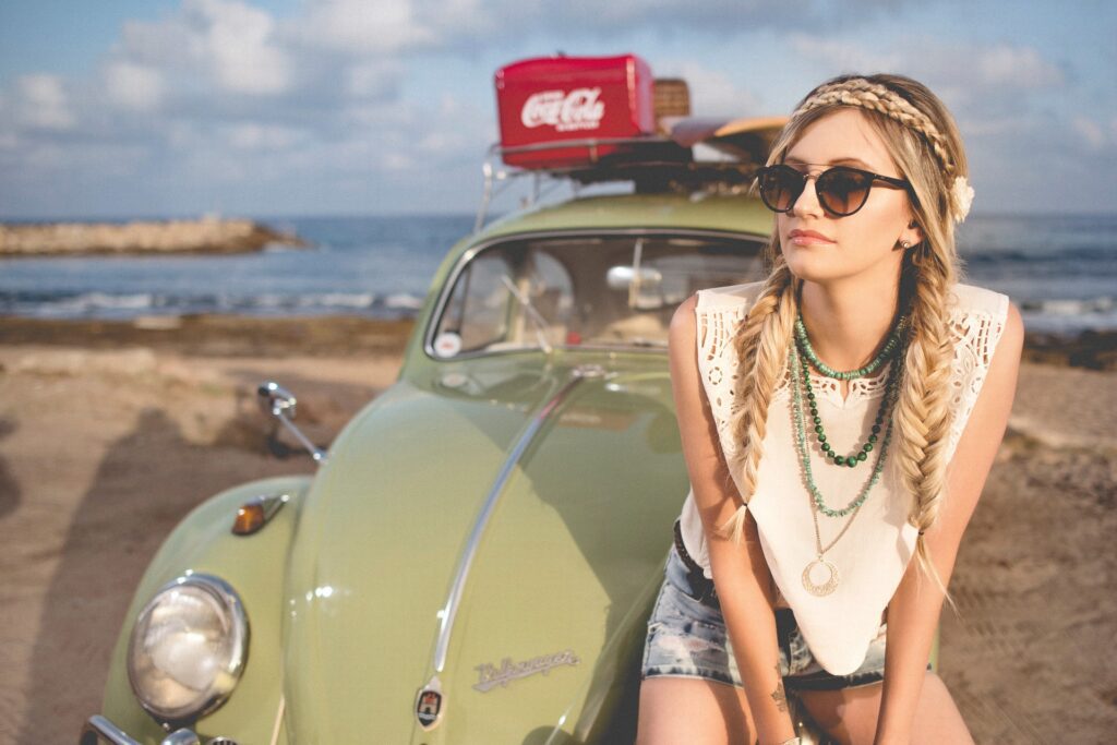 Young woman sitting on hood of car by the beach